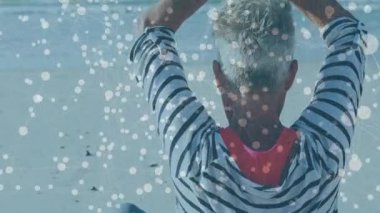 Kıdemli kadın kumlu sahilde kollarını kaldırıp dua mudrasına giriyor. Parlayan ışık noktalarının altında sakin bir zihin. Huzur, farkındalık, meditasyon, maneviyat, refah, dinginlik, kıyı