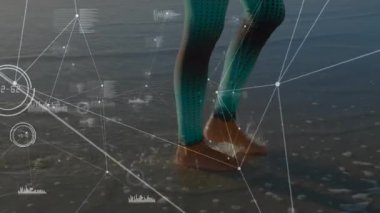 Sığ deniz suyuna basan, üzerinde deniz mavisi taytlar olan bir kadın canlı fitness izleme cihazını çalıştırıyor. Atletik, yaşam tarzı, dijital, teknoloji, açık hava, aktif, fitness