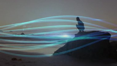 Işıldayan mavi kurdeleler, kıyı kayası alacakaranlığında çömelmiş bir kadına rehberlik ediyor. Sağlık odaklı. Siluet, sükunet, ambiyans, organik, mistik, meditasyon, uyum.