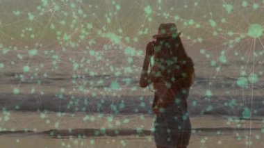 Kadın fotoğrafçı, güneş şapkası kaldırma kamerasını ayarlıyor, günbatımını teknolojiyle örtüyor. Deniz manzarası, gün batımı, manzara, dijital, cazibe, sükunet, seyahat tutkusu.