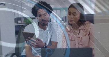 Tableti masadaki kadın meslektaşına doğru eğen bir adam, incelemek için ekranları veri örtüsü ile değiştiriyor. İşbirliği, takım çalışması, dijital arayüz, veri analizi, yenilik, profesyonel, modern