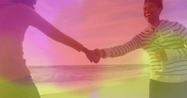 Gün batımında kumsala gelen çift, el ele tutuşup, gradyan örtüsü altında dönerek seyahat neşesini paylaşıyor. Romantizm, samimiyet, dinginlik, su, boş zaman, duygusal, ahenkli