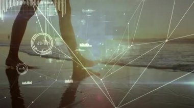 Gün batımında ıslak kuma adım atan bir kadın, teknolojik düğümleri ve silueti dalgalandıran veri göstergelerini başlatıyor. Teknoloji, yenilik, bağlantı, dijital, fütürizm, dinginlik, doğa