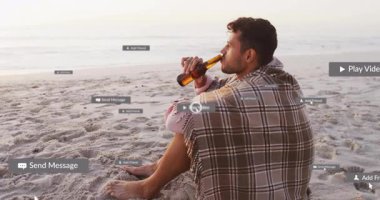 Gün batımı kumsalında bir yudum alan ve mesajlaşmanın gelişimini gösteren yüzen sosyal mesajları aktifleştiren adam. Huzur, bağlantı, sükunet, dijital arayüz, rahatlama, teknoloji, farkındalık