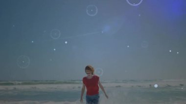 Kadın sörf yapıyor ve teknolojiyi vücudun etrafına yerleştiriyor, plaj görselleri sergiliyor. Deniz kenarı, dijital alarm, dinginlik, yenilik, macera, sükunet, doğa