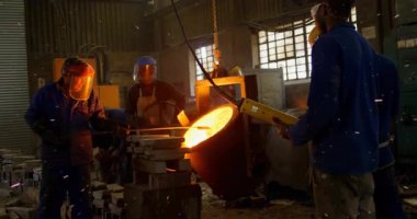 Dökümhane işletmecisi prangaya baskı yapıyor ve döküm için erimiş metali kalıba döküyor. Metal işleri, endüstriyel, işçilik, imalat, takım çalışması, güvenlik, süreç