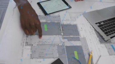 Tasarım ekibi tasarım boyutlarını doğrulayan cetvel ile tableti hizalayan tasarım planlarını açıyor. Mimari, işbirliği, yenilik, taslak, planlama, görselleştirme, kesinlik