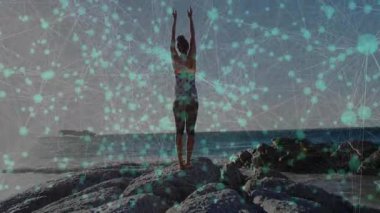 Güneşin doğuşu ilham verici fitness eğitmeni kayalık sahilde üstüste esneme egzersizi yapıyor, nabzı atıyor. Zirve, sağlık, canlılık, farkındalık, dinginlik, manzara, enerjik