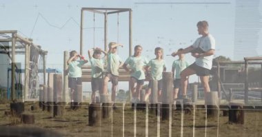 Koç bir sonraki tahta kütüğü işaret ederek kolunu kaldırıyor, grup olarak spor eğitimi için başını sallıyor. Açık hava, aktivite, antrenman, takım çalışması, motivasyon, atletizm