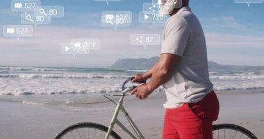 Sahilde duran adam medya simgelerini aktifleştiriyor, pazarlama ölçümlerini gösteren kum boyunca bisiklet sürüyor. Sahil, huzur, boş zaman, açık hava, minimalist, düşünceli, yaşam tarzı.