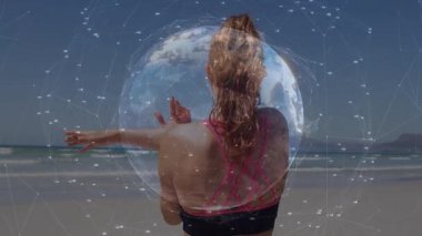 Sahilde kollarını uzatan bir kadın okyanusa bakıyor. Animasyon dünyası vücut geliştirme geriliminde görünüyor. Spor salonu, sağlık, animasyon, dijital, açık hava, sağlık, bağlantı