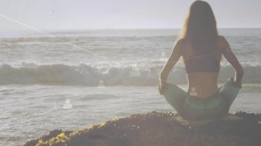 Yoga uygulayıcısı güneş doğarken kayalık okyanus üzerinde kollarını kaldırarak sağlık ağını çalıştırıyor. Meditasyon, sükunet, dijital, bağlantı, doğa, dinginlik, refah