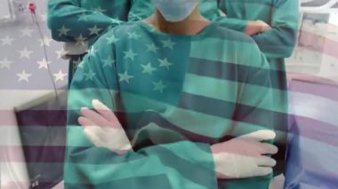 Kamera, ABD bayrağı soluklaşırken ameliyathanede çapraz kollu cerrahi ekibi gösteriyor. Tıbbi, takım çalışması, profesyonel, dayanıklılık, klinik, sağlık, birlik