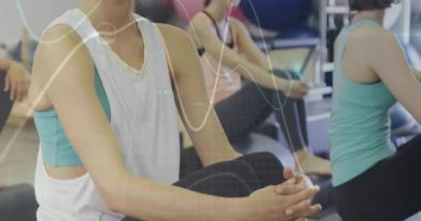 Pilates reformatöründe dizini kavrayan bir kadın grup esneme hareketleri yaparken dalga kaplamasını etkinleştiriyor. Spor, sağlık, grup çalışması, esneme, hareketlilik, motivasyon, egzersiz