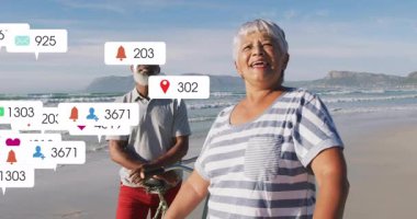 Woman raising smartphone for beach selfie with partner by bike and social media icons multiplying. Outdoors, leisure, photography, connection, tranquility, adventure, technology