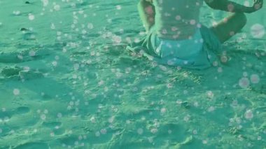 Kameralar kumlu sahili tarıyor ve kıdemli yogilerin okyanusa doğru ışık küreleriyle meditasyon yaptığını gösteriyor. Dinginlik, rahatlama, farkındalık, sahil, huzur, maneviyat, refah.