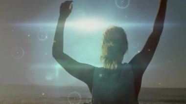 Gün batımında kumsalda kollarını kaldıran bir kadın esneme hareketleri sırasında titreşen ışık örtülerini tutuşturuyor. Siluet, sükunet, hareket, canlandırma, güçlendirme, doğal, minimalist