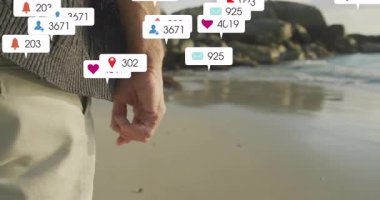 Kıdemli adam dalgalara bakıyor ve elinde büyümeyi gösteren sosyal medya bildirimlerine neden oluyor. Mutluluk, tefekkür, dinginlik, bağlantı, dijital, minimalizm, yansıma