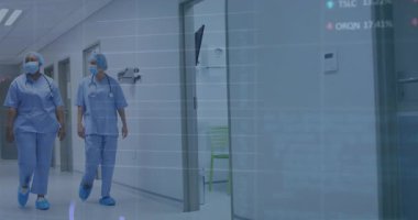 Hastane koridorunda yürüyen iki hemşire hastanın hayati değerlerini takip eden tıbbi veri tablolarını aktifleştiriyor. Sağlık, takım çalışması, analitik, profesyonellik, klinik, yenilik, tıbbi