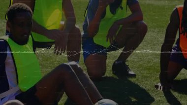 Erkek futbolcular sahada koçun yorumlarını duyuyorlar ve neon önlükleri yüzen dalga şeklinde ayarlıyorlar. Atletizm, takım çalışması, motivasyon, açık hava, canlı, eğitim, birlik