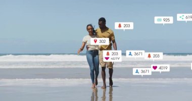 Sahilde kol kola yürüyen bir çift, sosyal medya simgelerinin büyüyüp azaldığını gösteriyor. Romantik, kıyı şeridi, bağlılık, dijital, açık hava, canlı, bağlantı