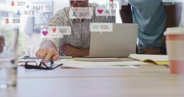 Sosyal medya simgeleri iş masasının etrafında çarparken adam belgeleri işaret ediyor ve ekibin odaklanmasını sağlıyor. İşbirliği, takım çalışması, dijital, iletişim, yenilik, profesyonel, beyin fırtınası