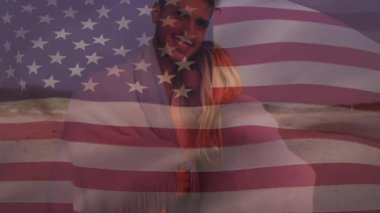 Sahile ayak basan çift, ABD bayrağının ufukta kayboluşunu vatansever pazarlama için kucaklaşmasını tetikliyor. Romantik, huzur, vatanseverlik, yumuşak ışık, birlik, sahil şeridi, şefkat