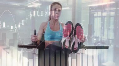 Makinenin üzerinde dizlerini kaldırırken tutamakları sıkıca kavrayan ve kaslarını esneten, finans tablolarını gösteren bir kadın. Fitness, egzersiz, sağlık, yenilik, motivasyon, veri