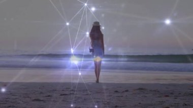 Woman pausing on sand then stepping into surf for travel content with pulsing tech overlay fading. Beach, waterfront, sunset, digital art, serenity, exploration, peaceful