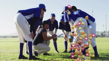 Beyzbol koçu sahada diz çöküp oyuncuların toplanıp emojileri yuvarladıklarını not alıyor. Koçluk, takım toplantısı, strateji, sportmenlik, atletizm, açık hava, takım çalışması.