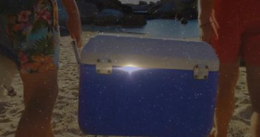 Çekici saplı adamlar, hareketli mercek fişekleri ile seyahat etmek için plajdan kıyıya serinletici taşırlar. Tatil, boş zaman, açık hava, macera, gündelik, doğa, eğlence