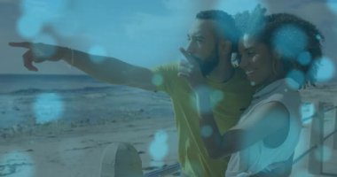 Adam kolunu kaldırıp ufuk çizgisindeki kadını işaret ediyor. Bokeh seyahat pazarlamasıyla plaj korkuluklarında yansıtıyor. Romantik, deniz kenarı, bağlantı, eğlence, dinginlik, canlılık, doğa