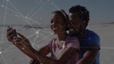 Akıllı telefonu kaldıran bir kadın ve teknoloji tanıtımı için plaj ağı oluşturan bir erkek. Romantik, bağlantı, teknoloji, dijital, sosyal, açık hava, modern