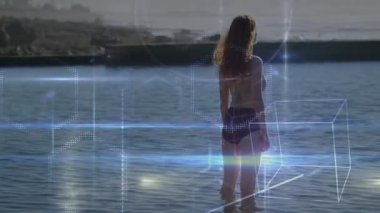 Diz boyu kıyı suyuna adım atan ve teknolojik görüntüler için dalga formlarını ve küpleri etkinleştiren bir kadın. Modern, fütüristik, soyut, dijital, deniz, huzur, yenilik