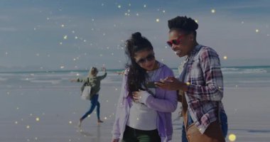 Işıltı efektiyle dans eden iki arkadaş, teknik demo arkadaşı için ıslak kıyıda telefon dinlerken duraklıyor. Açık hava, yaşam tarzı, rahat, canlı, kutlama, boş zaman, bağlantı