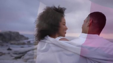 Sahilde gün batımında kucaklaşan bir çiftin önünde Fransız bayrağının soluşunu gösteren bir seyahat reklamı. Romantizm, sahil, gün batımı, dinginlik, bağlantı, şefkat, manzara