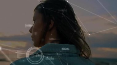 Kadın gün batımında elini kaldırıyor ve dijital ağı etkinleştiriyor. Veri düğümlerini gösteriyor. Dijital, düşünceli, sakin, fütüristik, sahil, sakin, bağlantı