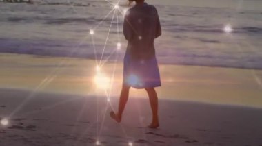 Islak kumda yürürken, okyanusa bakarken topuk kaldıran kadın teknolojiyi çalıştırıyor. Yalnızlık, huzur, bağlantı, dijital, manzara, yansıma, sükunet