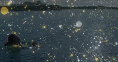 Denizde yüzen ve altın bokeh ile yüzen kameraman kadına doğru dönüyoruz. Dinginlik, su, rahatlık, akıcılık, sükunet, kıyı, yansıtıcı