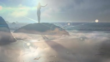 Şafak vakti kumsalda kollarını kaldıran bir kadın teknoloji ağının gökyüzü ve kum boyunca genişlemesine neden oluyor. Siluet, gündoğumu, bağlantı, fütürizm, dinginlik, meditasyon, soyut