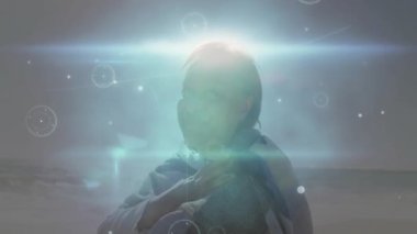 Kıyı şeridinde kıdemli bir kadın, elinde şalla parıltı sönerken ve iyileşme örtülerini aktifleştirirken. Dinginlik, farkındalık, sükunet, meditasyon, rahatlama, kıyı, çağdaş