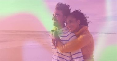 Kol kaldıran ve plaj kenarında sarılan bir kadın pastel gökyüzü altında romantik bir yaşam tarzını paylaşıyor. Romantizm, samimiyet, şefkat, uyum, dinginlik, bağlantı, açık hava