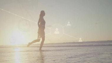 Güneş ışığında yürüyen bir kadın dijital örtüyü etkinleştiriyor ve su şebekesini tekmeliyor. Deniz kenarı, siluet, teknoloji, bağlantı, boş zaman, kıyı, canlı