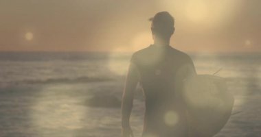 Gün doğumunda kıyıda yürüyen sörfçü sörf seansına hazırlanan dalgaları tarıyor. Macera, sükunet, sahil, sükunet, uygunluk, keşif, doğa