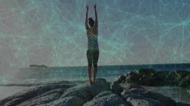 Kadın, taşlı okyanus çıkıntısında kollarını kaldırıyor ve animasyon ada ikonuyla yoga yapıyor. Deniz manzarası, fitness, meditasyon, açık hava, canlılık, dinginlik, aktif giysi