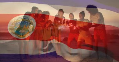 Gün batımı sahilinde turizm için kıvılcımlar saçan bir grup. Kosta Rika bayrağı dalgalanarak dalgalanacak. Kutlama, dostluk, günbatımı, plaj, çok kültürlü, sıcak, dinginlik