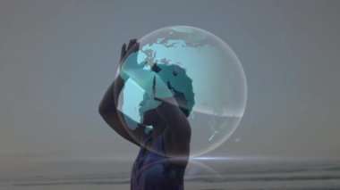 Okyanus kıyısında kollarını kaldıran bir kadın, dijital küreye sağlık için girdap şeklinde ışık yollarıyla güç veriyor. Ruhani, sağlıklı, huzur, farkındalık, fütüristik, dinginlik, canlılık