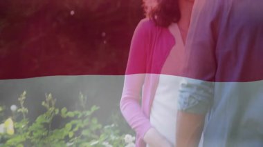 Sağlık kampanyasında gülümseyen bir kadın, güneşli bahçede kollarını kaldırarak sarılan bir adama el sallıyor. Romantizm, şefkat, samimiyet, açık hava, bereketli, canlı, doğal