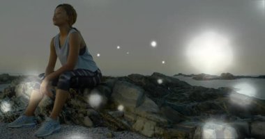 Gün batımında kayalık kıyı şeridine yaklaşan bir kadın, parlayan ışıklarla soluklanmak için soluklanıyor. Kıyı, meditasyon, sükunet, alacakaranlık, aktif giysi, farkındalık, sükunet