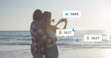 Günbatımı plaj selfie 'si için akıllı telefonları dinleyen ve etrafta sosyal medya simgeleri uçuşan bir çift. Romantizm, teknoloji, bağlantı, kutlama, sükunet, coşku, yaşam tarzı